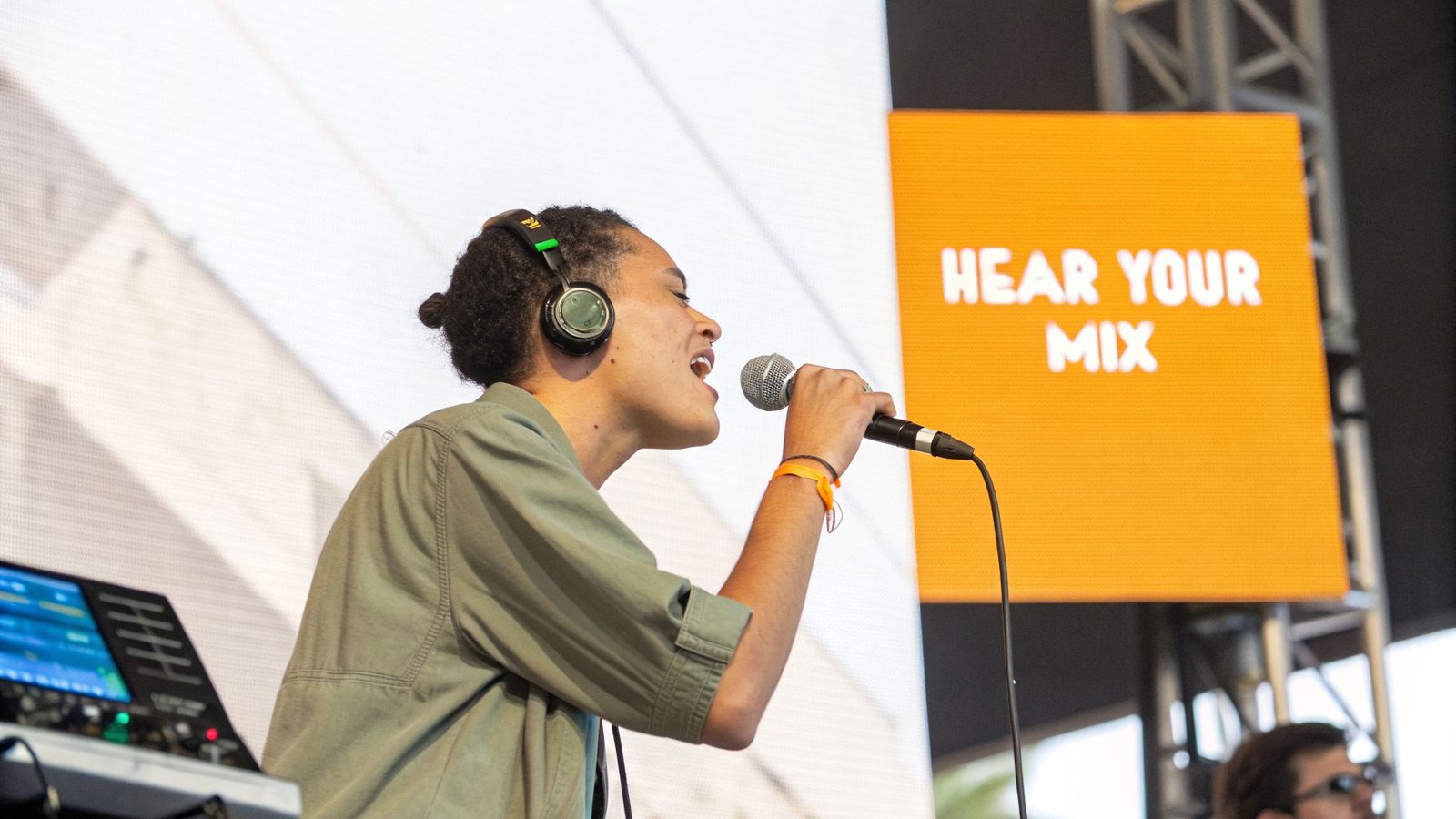 A person with headphones and a microphone performs on stage, with a 'HEAR YOUR MIX' screen in the background.