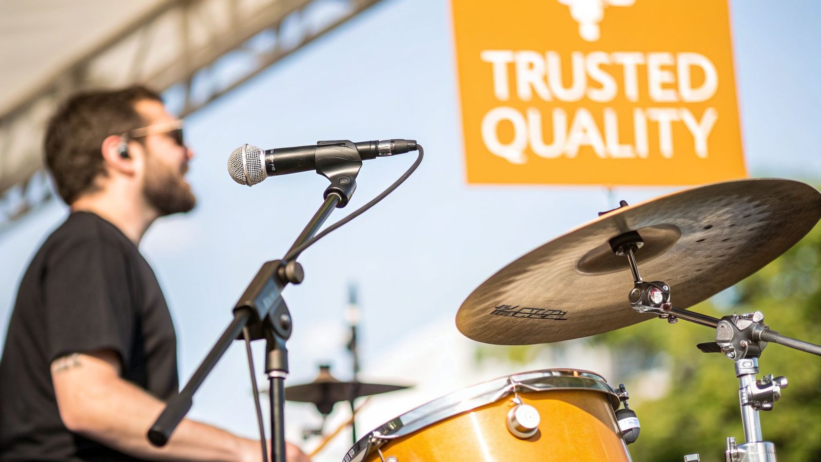 A close-up of a drum kit microphone and cymbal on stage, with a blurred drummer.